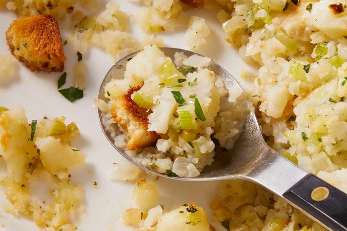 Close-up of a spoonful of Potato Stuffing lifted from the dish, showing tender potatoes, bread pieces, and herbs.
