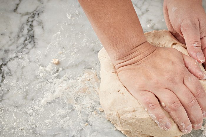 Hands kneading dough on a floured marble surface, preparing it for baking.