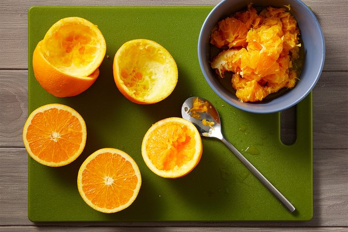 Overhead shot of halved and hollowed oranges on a green cutting board beside a spoon and a bowl filled with the scooped orange pulp;