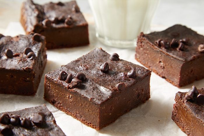 Closeup shot of hidden veggie brownies topped with chocolate chips served with a glass of milk;