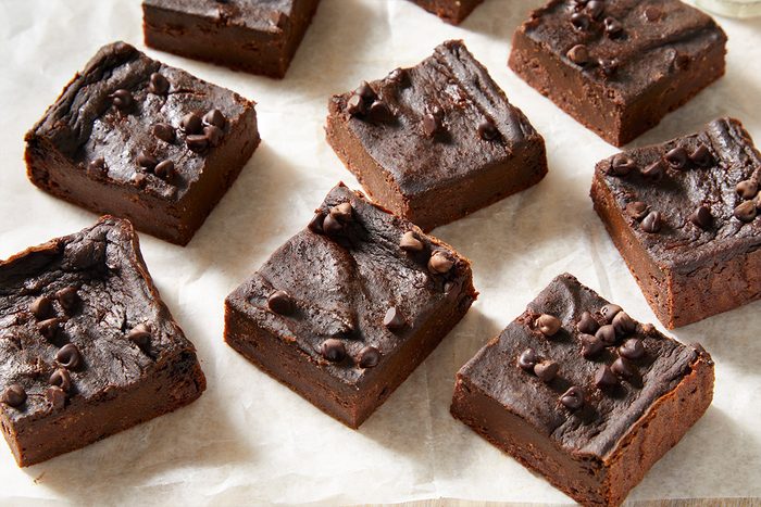 Close shot of sliced hidden veggie brownies topped with chocolate chips on parchment paper;