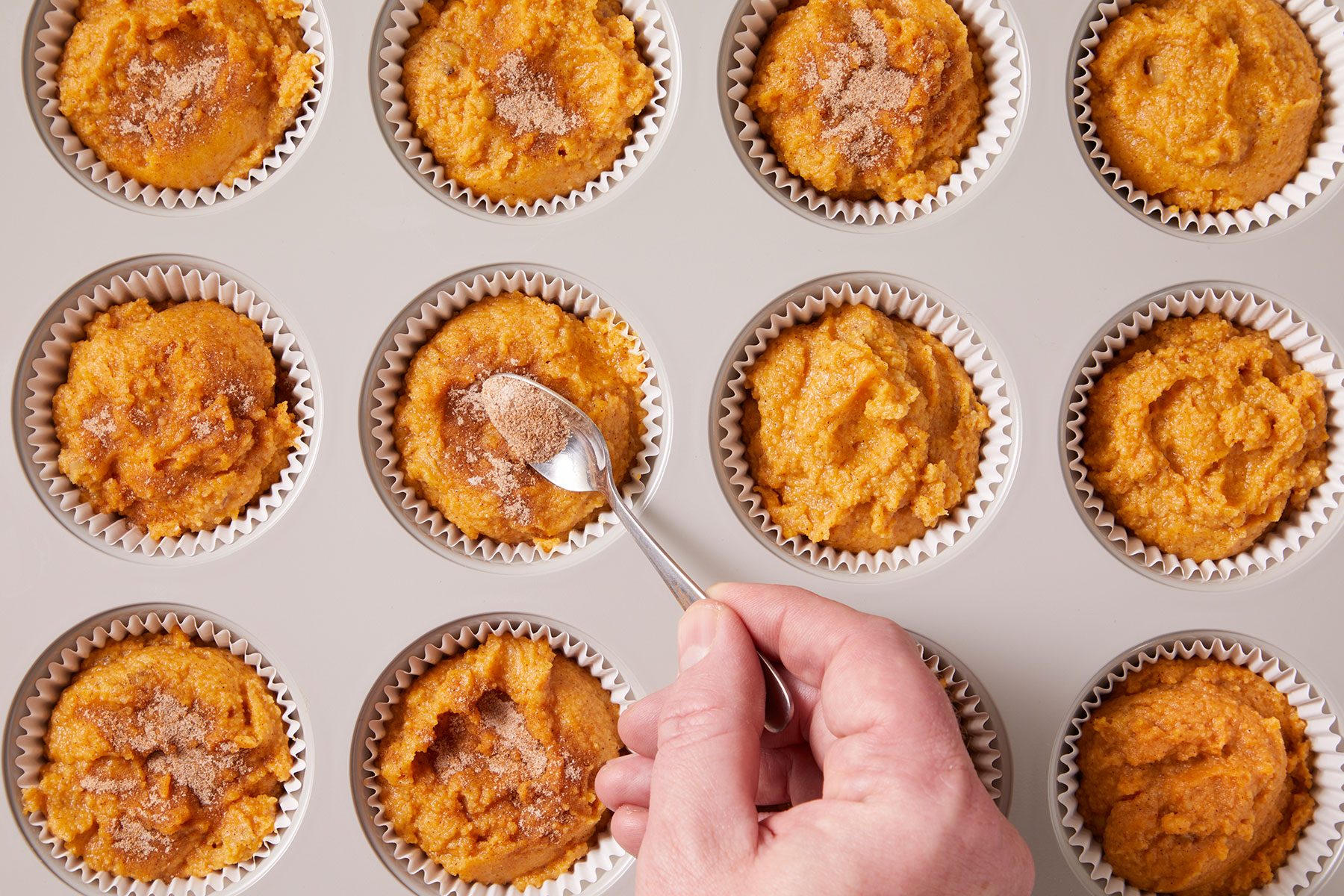 Sprinkling cinnamon and sugar mixture on unbaked muffins.