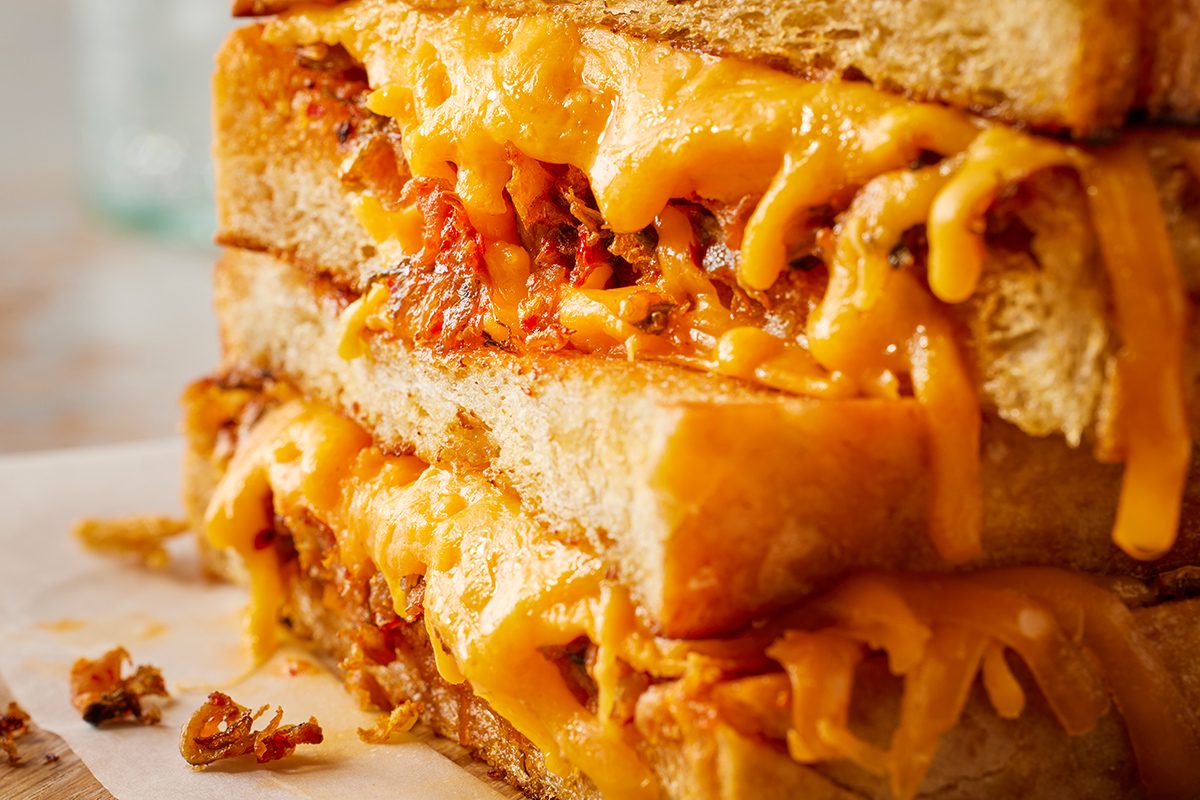 Close-up of a grilled cheese sandwich with melted cheddar cheese and caramelized onions, stacked on top of each other, showing gooey cheese stretching between layers of toasted bread.