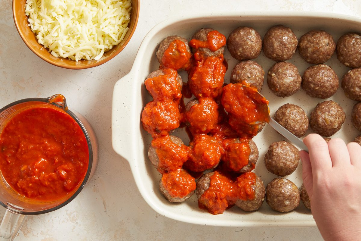 baked meatballs being covered with marinara sauce