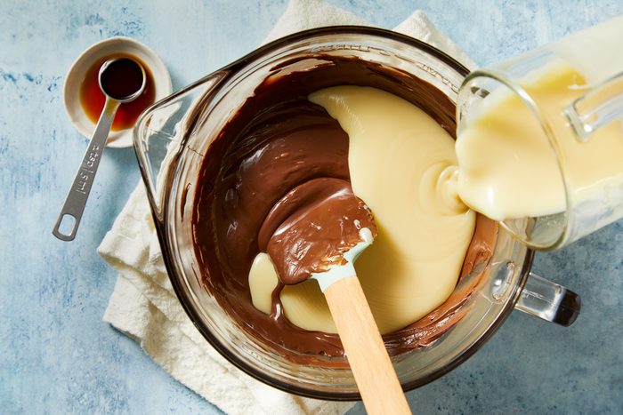 sweetened condensed milk being poured into melted chocolate mixture